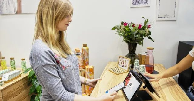 A woman uses a tablet to make a payment in a stylish Berlin store, featuring modern decor and eco-friendly products.