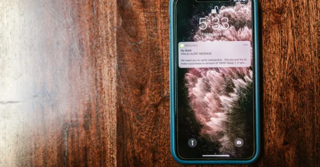 Close-up of a smartphone displaying a fraud alert message on a wooden table.