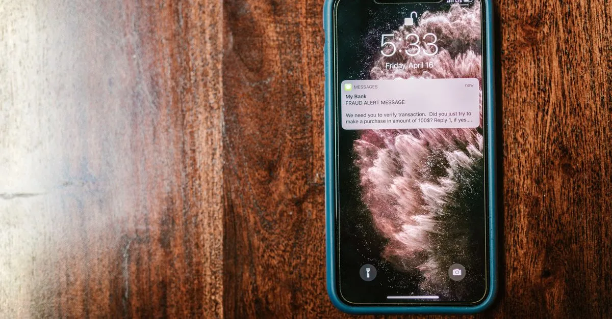 Close-up of a smartphone displaying a fraud alert message on a wooden table.
