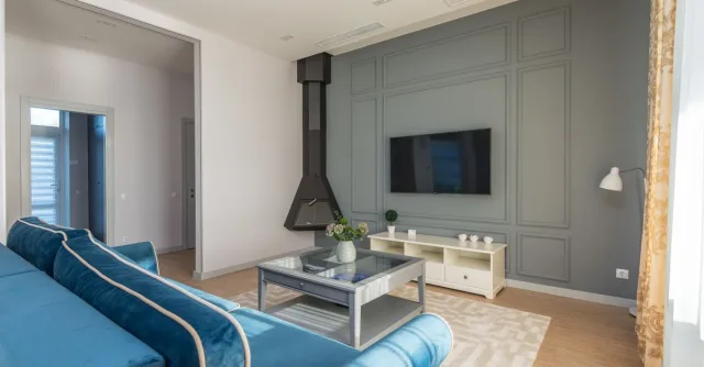 A stylish living room featuring a blue couch, wall-mounted TV, and elegant decor.