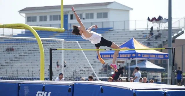 A male high school athlete executing a high jump during a track and field event, outdoors.