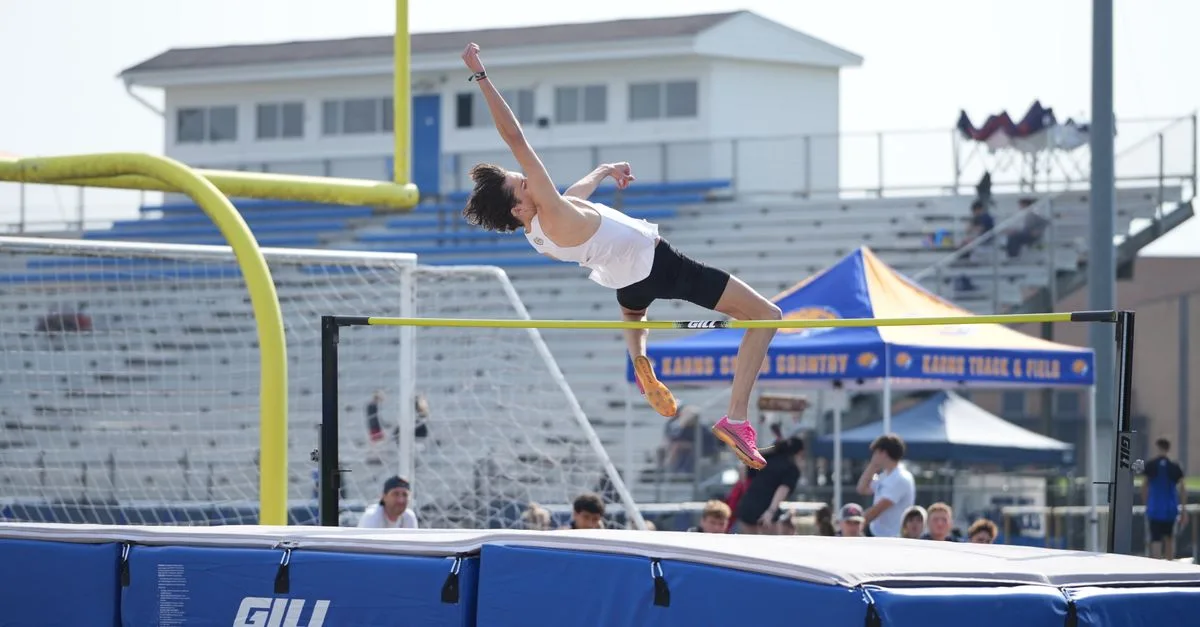 A male high school athlete executing a high jump during a track and field event, outdoors.