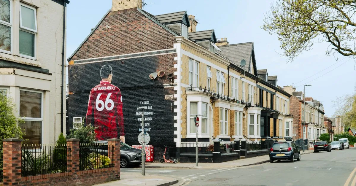 Urban street scene in Liverpool featuring a prominent mural of Trent Alexander-Arnold.