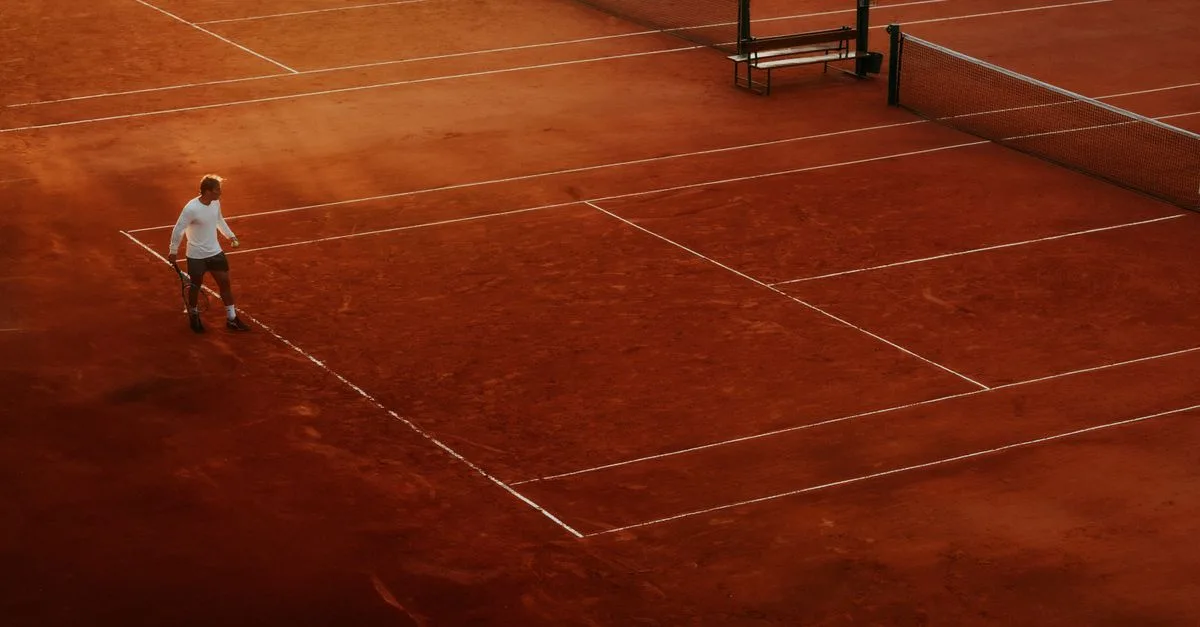 Aerial shot of a tennis player on a clay court during daytime, highlighting the sport's dynamic environment.