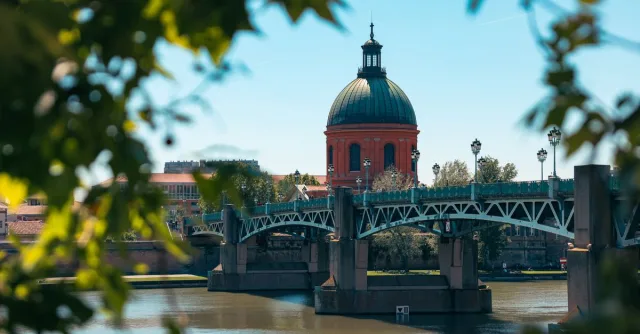 Scenic view of Pont Saint-Pierre and red dome in Toulouse, France framed by leaves.