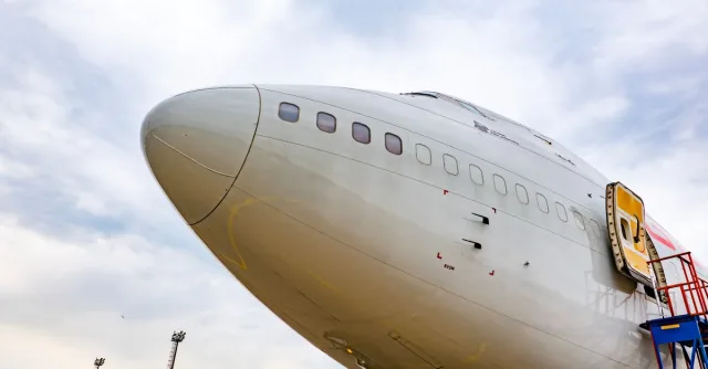 Detailed view of a commercial airplane's nose with an open hatch under a vibrant sky.