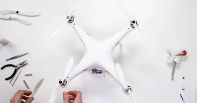 Hands assembling a quadcopter drone on a white surface with various tools around.