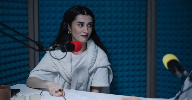 A woman in a podcast studio with microphones and headphones, focused on a discussion.