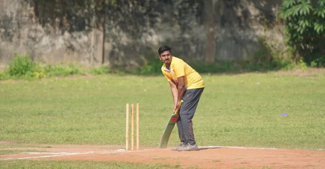 A cricketer in a yellow jersey prepares to bat during a sunny day match.