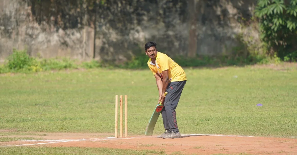 A cricketer in a yellow jersey prepares to bat during a sunny day match.