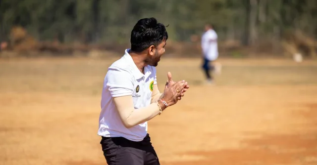 A dynamic shot of a cricketer clapping during an outdoor match on a sunny day.