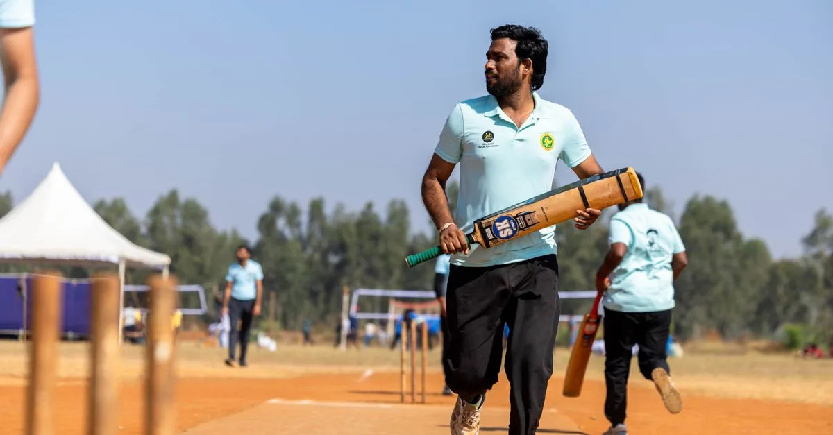 Cricketer with bat ready on sunny day outdoor field, sporting event.