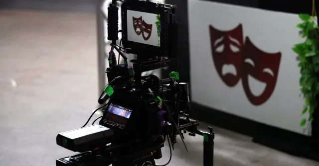 Professional film camera capturing theater performance showing drama and comedy masks.