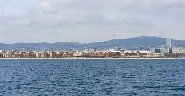 Stunning panoramic view of Barcelona coastline with urban skyline and distant hills under a cloudy sky.