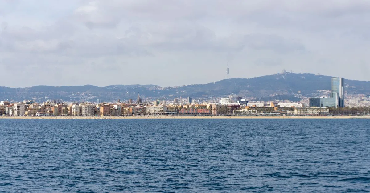 Stunning panoramic view of Barcelona coastline with urban skyline and distant hills under a cloudy sky.