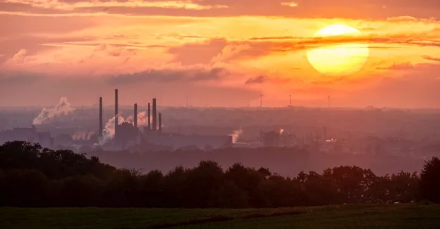 A stunning sunset over an industrial landscape with smoke rising from factory chimneys.