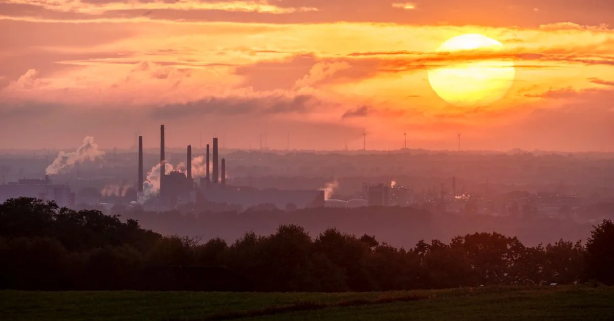 A stunning sunset over an industrial landscape with smoke rising from factory chimneys.