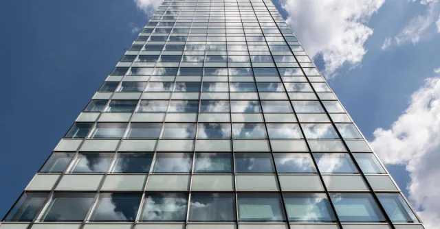 A sleek Hamburg skyscraper with glass facade reflecting clouds on a sunny day.
