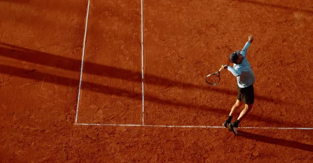 A dynamic shot of a tennis player serving on a clay court during sunset.