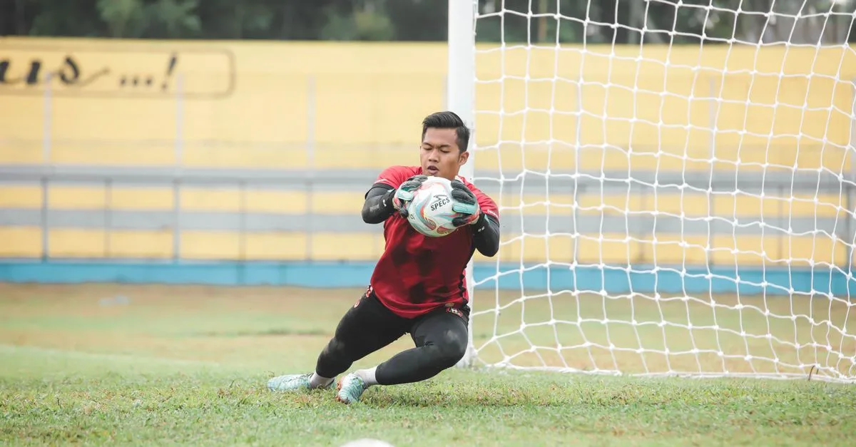 A soccer goalkeeper making a dynamic save during a game outdoors in Jakarta, Indonesia.