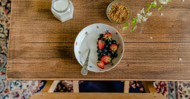 Aerial view of breakfast setup with a bowl of fresh fruits, milk, and granola on a wooden table.