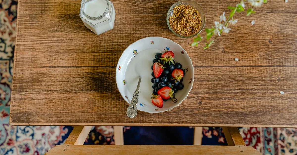 Aerial view of breakfast setup with a bowl of fresh fruits, milk, and granola on a wooden table.