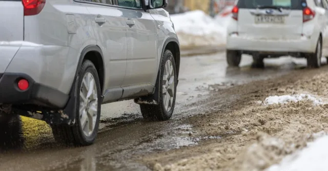 Two cars driving cautiously on a slushy, snowy road during winter.