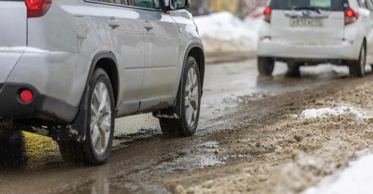 Two cars driving cautiously on a slushy, snowy road during winter.