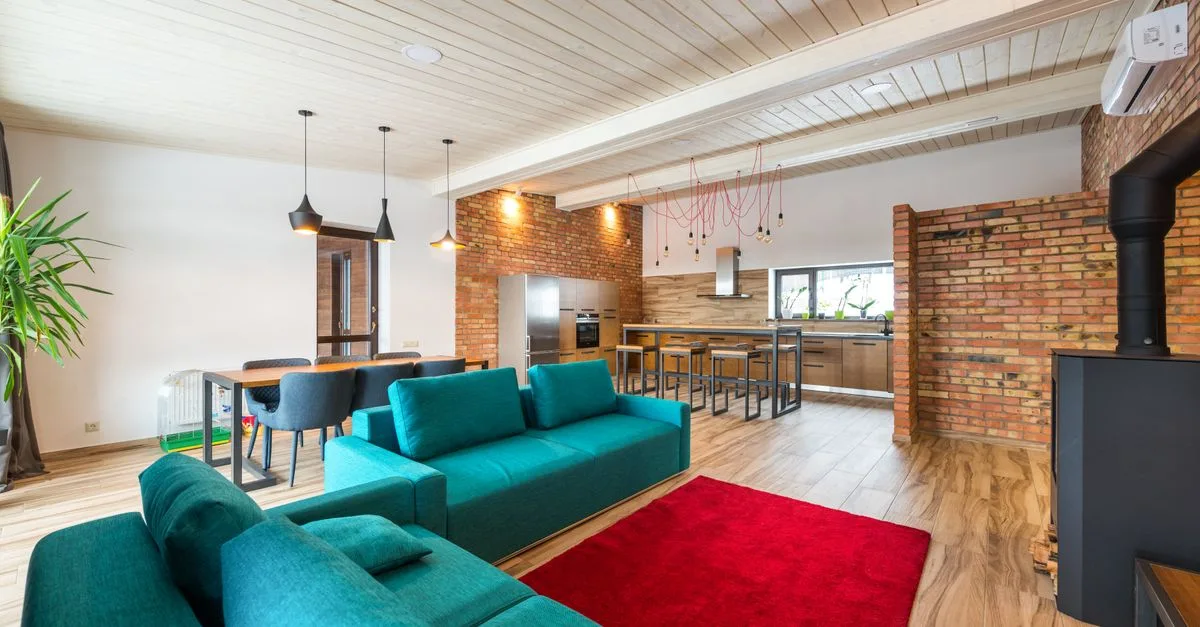 Spacious modern living room featuring brick walls, teal sofa, and red rug.