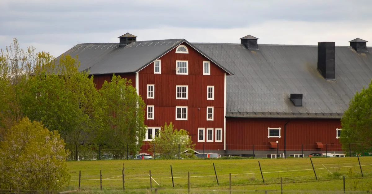 Scenic view of a classic red Swedish barn surrounded by lush greenery in Jönköping, Sweden.
