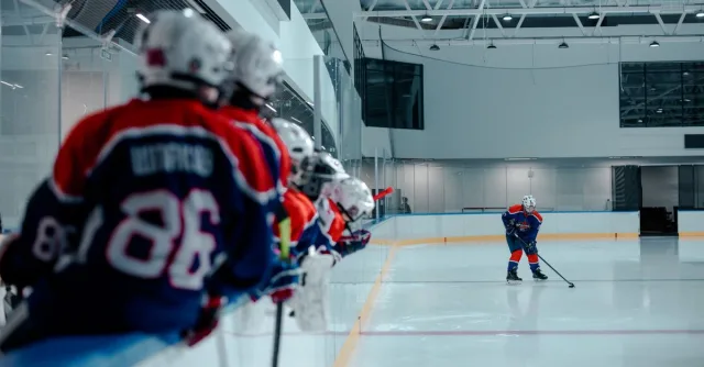 Ice hockey players on the rink, with a team in the foreground and an active player practicing.