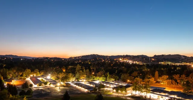 A serene twilight aerial view of a town with illuminated buildings against a blue sky.