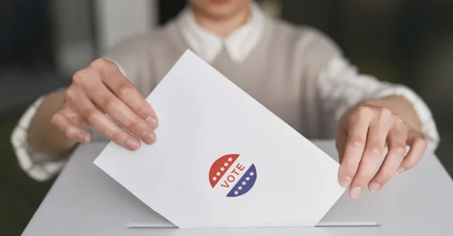 A person casting a vote by placing a ballot into a ballot box, symbolizing democratic participation.