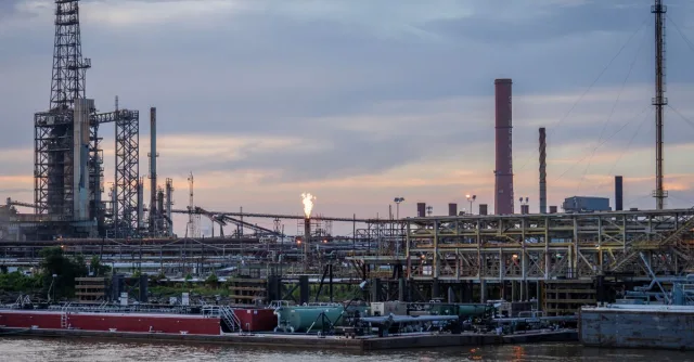 A large industrial refinery complex next to a river with a sunset backdrop.