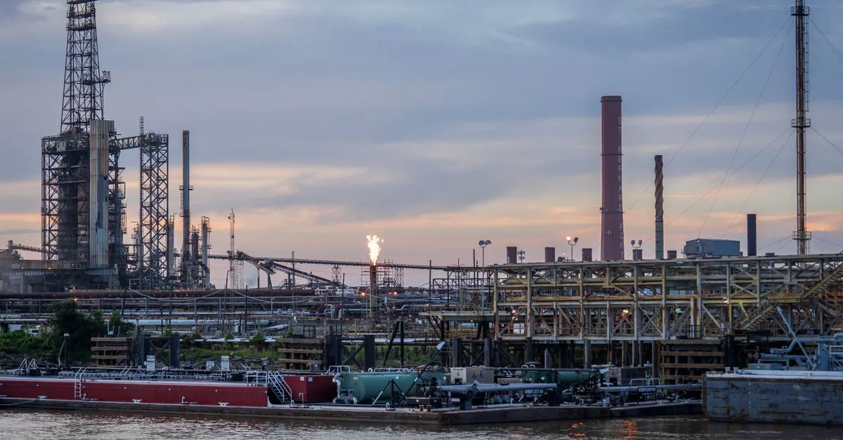 A large industrial refinery complex next to a river with a sunset backdrop.