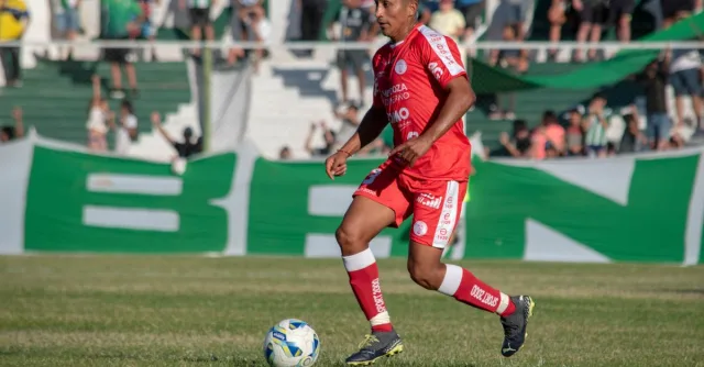 Soccer player in red uniform dribbling a ball during a match on a sunny day.