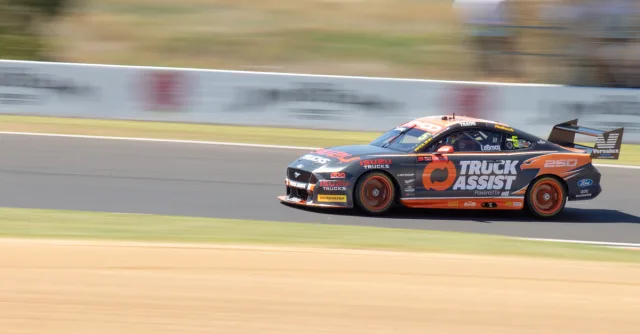 A racing car speeds around Mount Panorama track, showcasing dynamic motion and precision.