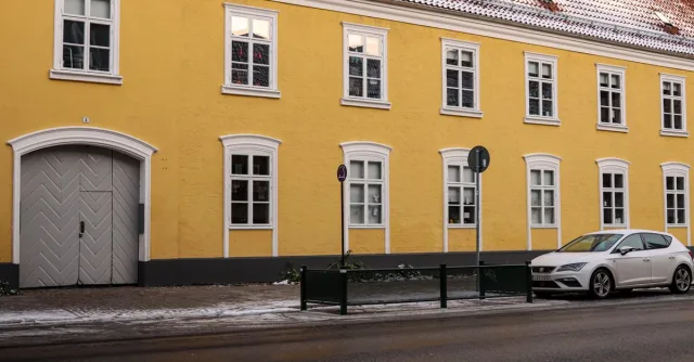 Charming yellow building in Malmö with snow-dusted roof and parked car.