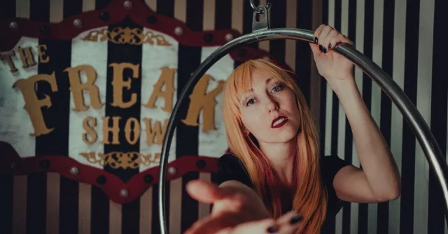 A woman posing artistically with a hoop against a vintage "Freak Show" sign.