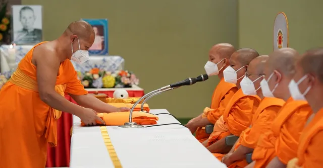 Masked Buddhist monks participating in a traditional ceremony with folded robes.