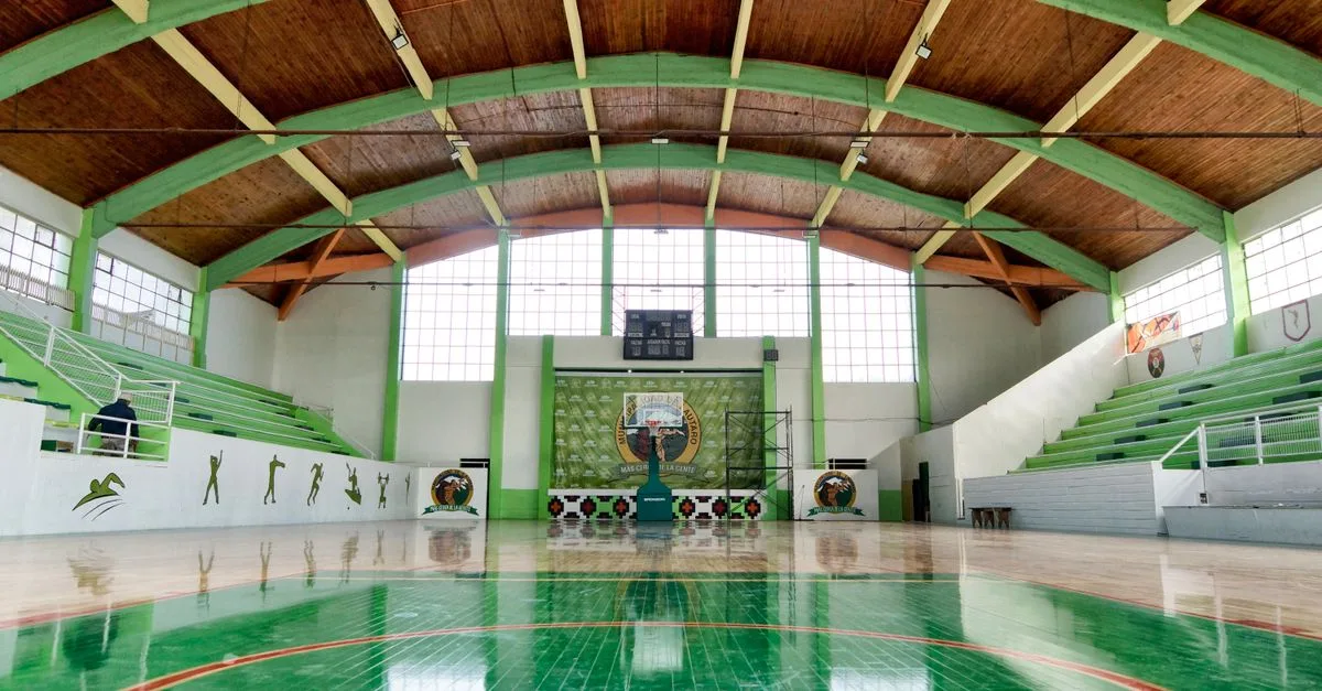 Wide view of an empty indoor basketball court in Lautaro, Chile with green details.