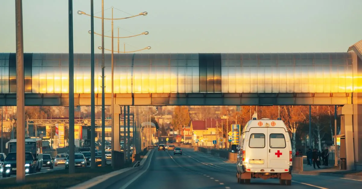 Ambulance driving through urban area on a road under sunset lighting.