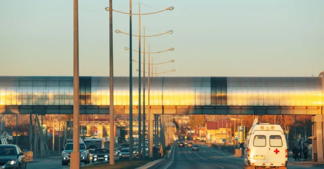 A busy urban highway scene with an ambulance and cars at sunset, showcasing modern architecture.