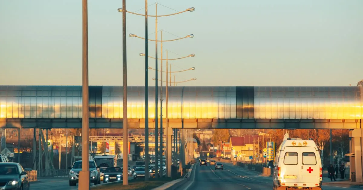 A busy urban highway scene with an ambulance and cars at sunset, showcasing modern architecture.
