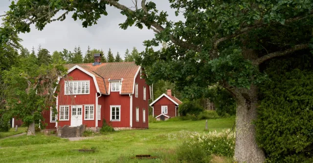 Idyllic red wooden house in a serene Swedish landscape surrounded by lush greenery.