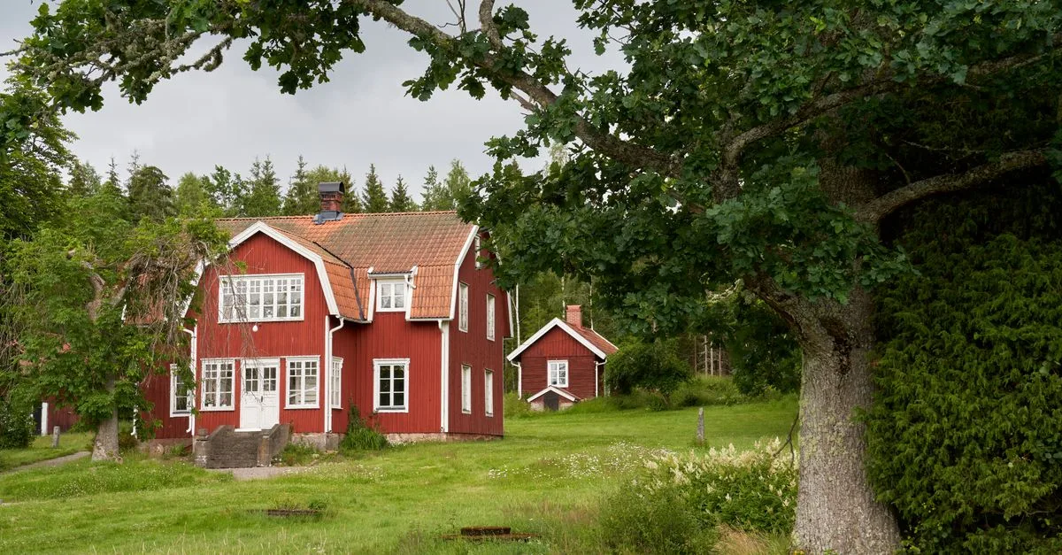 Idyllic red wooden house in a serene Swedish landscape surrounded by lush greenery.