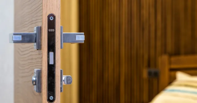 Opened doorway with lock and simple metal handle in light room with wooden bed