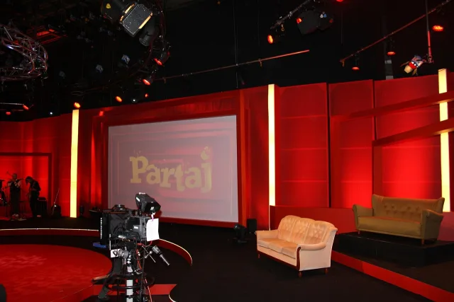 A modern, brightly lit television studio stage with comfortable chairs arranged for an interview.