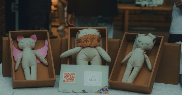 A close-up of handmade plush toys in cardboard boxes displayed indoors at a craft event.