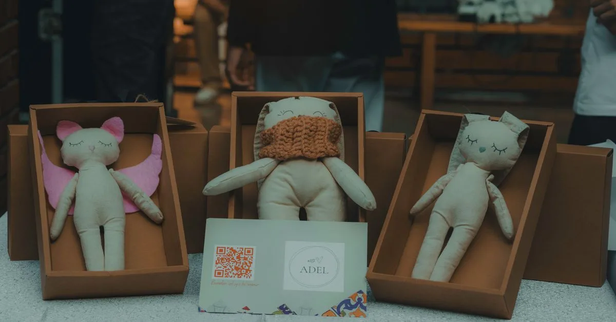 A close-up of handmade plush toys in cardboard boxes displayed indoors at a craft event.